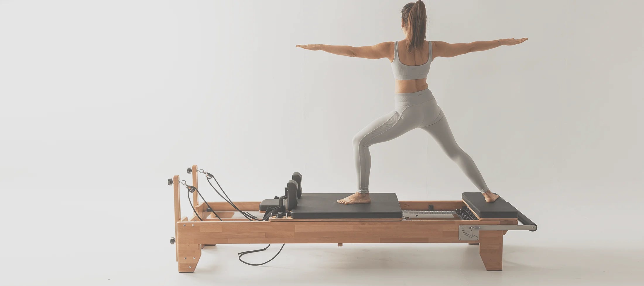 Woman exercising on an Almafit Pilates reformer machine against a plain background